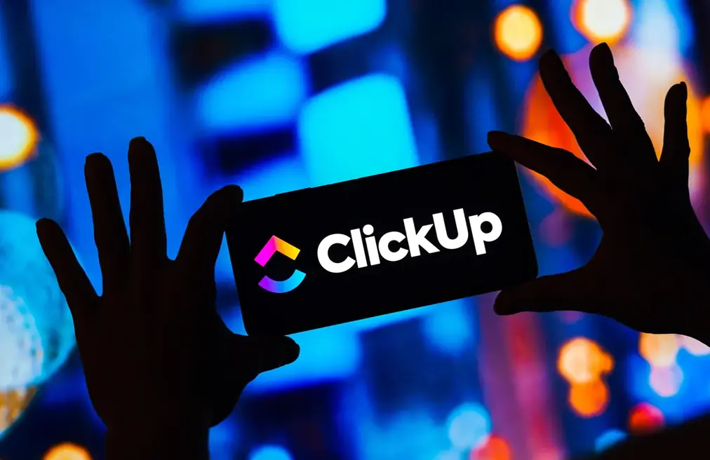 Painel iluminado com o logotipo do ClickUp e mãos em contraluz